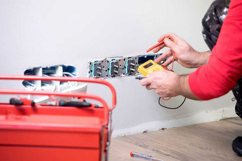 électricien mesurant la tension d'une prise avec un multimètre